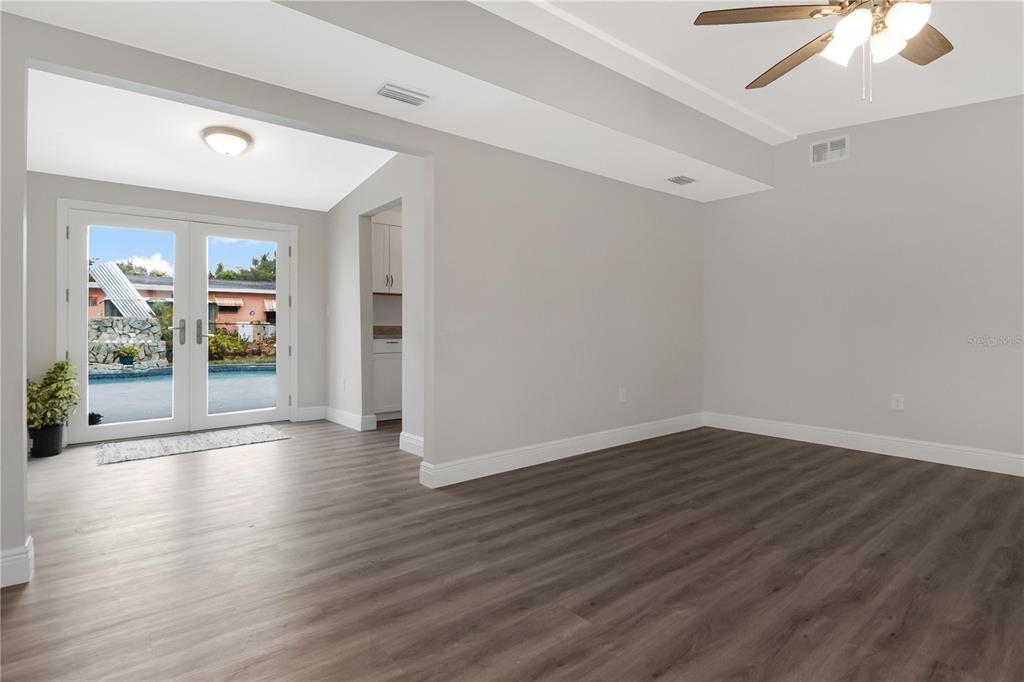 An interior view of a living room with wood-look flooring and glass doors to a pool — 2216 E 109TH AVENUE, TAMPA, FL