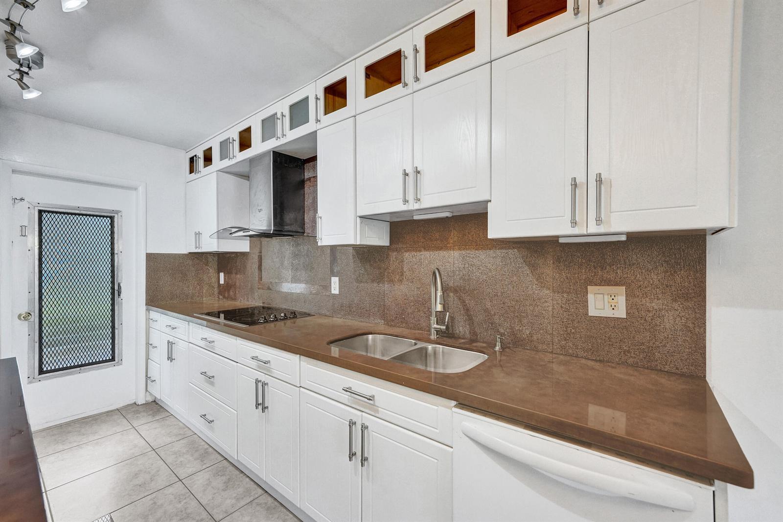 A kitchen features white cabinets, brown countertops, a stainless steel sink, and a glass-paneled door — 600 SE 2nd Avenue # K2, Deerfield Beach FL 33441, DEERFIELD BEACH, FL