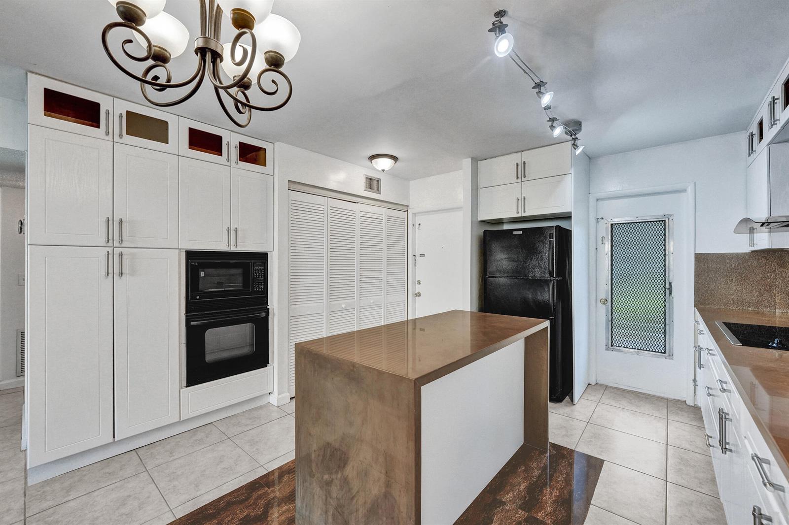 A kitchen features white cabinetry, a brown island, black appliances, and a chandelier — 600 SE 2nd Avenue # K2, Deerfield Beach FL 33441, DEERFIELD BEACH, FL