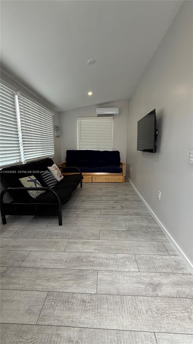 A room with gray wood-look tile flooring, two futons, a wall-mounted television, and blinds — 65821 Overseas Hwy # 314, Long Key FL 33001, LONG KEY, FL