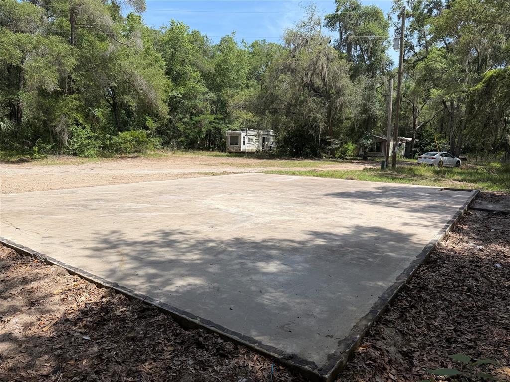 A large, rectangular concrete slab sits in a wooded lot near a parked trailer — 1628 S PALM AVENUE, HOMOSASSA, FL
