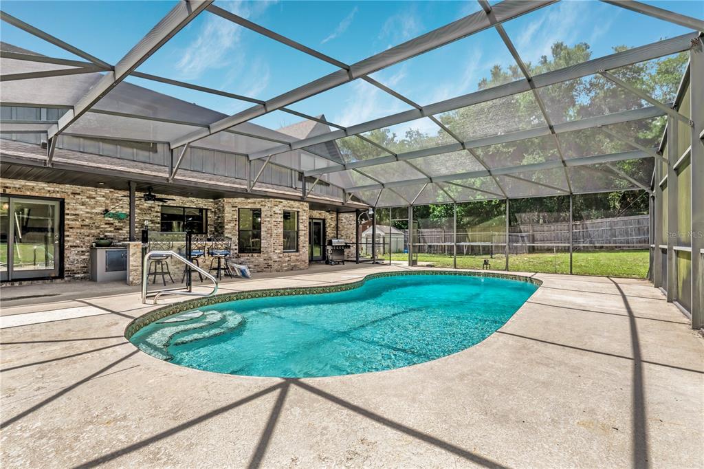 A screened-in patio features a swimming pool, outdoor kitchen, and concrete deck — 1375 LOUIS COURT, DELAND, FL