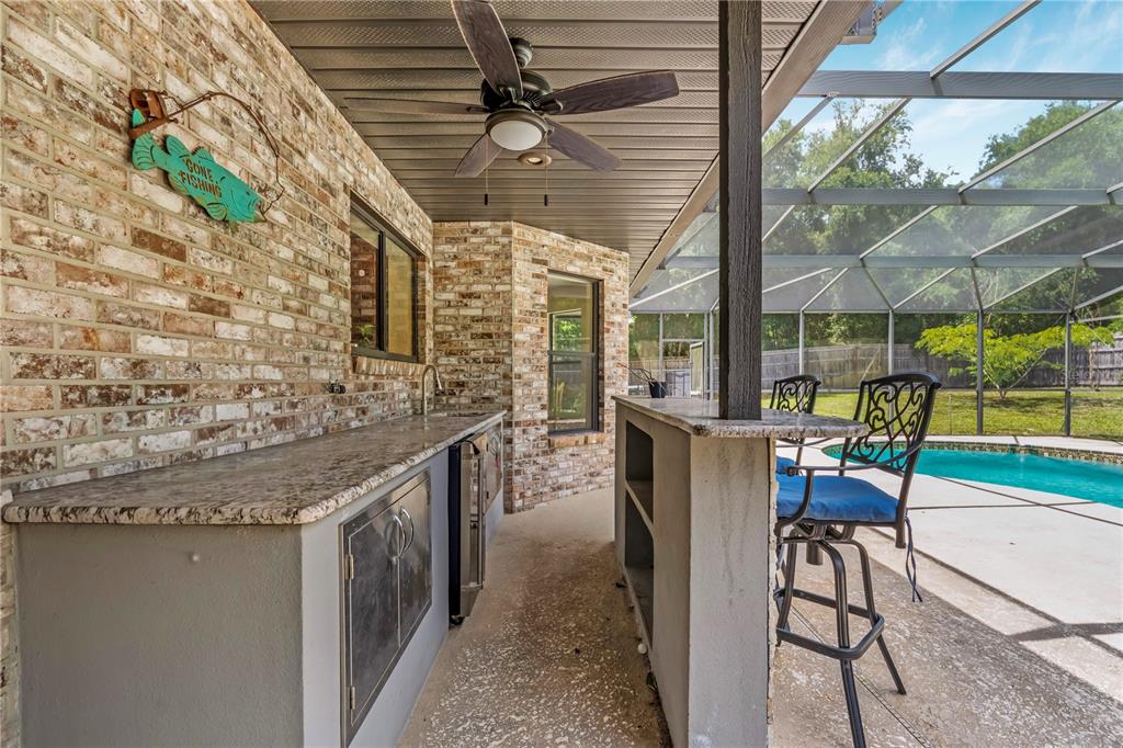 An outdoor kitchen with a granite countertop and bar seating overlooks a screened-in swimming pool — 1375 LOUIS COURT, DELAND, FL