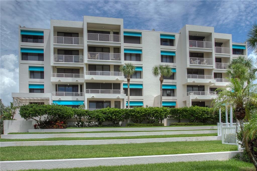A multi-story white apartment building with blue awnings and tiered grassy landscaping in front — 2109 GULF OF MEXICO DRIVE UNIT 1402, LONGBOAT KEY, FL