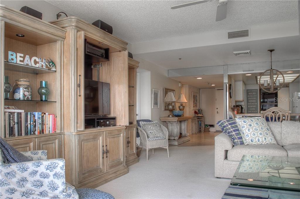 A living room features a large wooden entertainment center, a sofa, and a wicker chair — 2109 GULF OF MEXICO DRIVE UNIT 1402, LONGBOAT KEY, FL