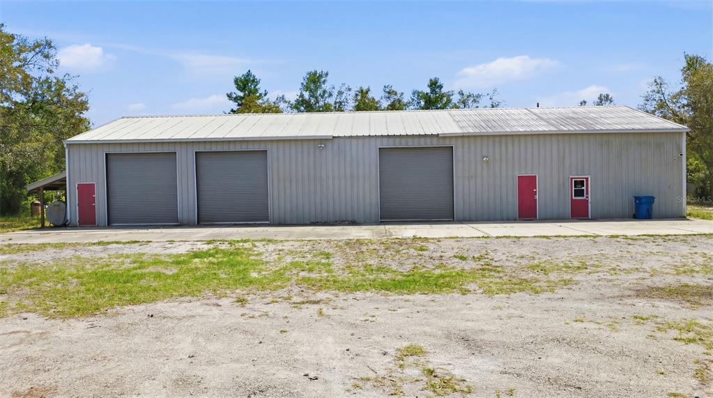 A long, single-story metal warehouse building features three roll-up doors and two red entry doors — 4155 MARSH ROAD, DELAND, FL
