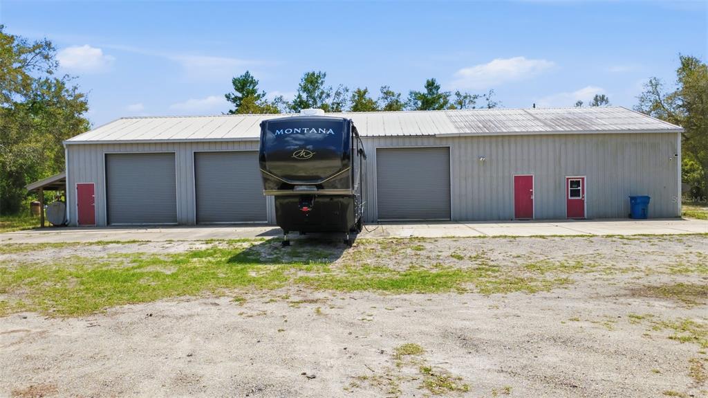 A large metal workshop building features three roll-up doors and a parked Montana fifth-wheel trailer — 4155 MARSH ROAD, DELAND, FL