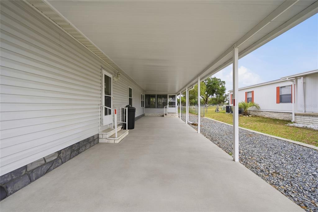 A long concrete carport with a white metal roof runs alongside a mobile home — 8401 WEATHERFORD AVENUE, BROOKSVILLE, FL