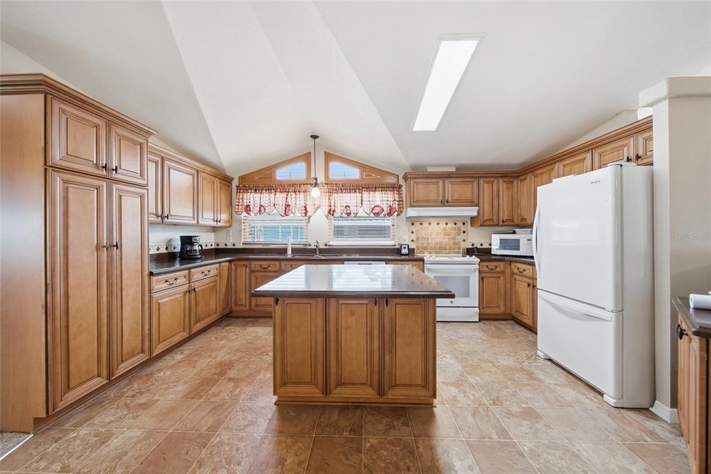A kitchen features wood cabinets, a central island, tile flooring, and a vaulted ceiling — 8401 WEATHERFORD AVENUE, BROOKSVILLE, FL