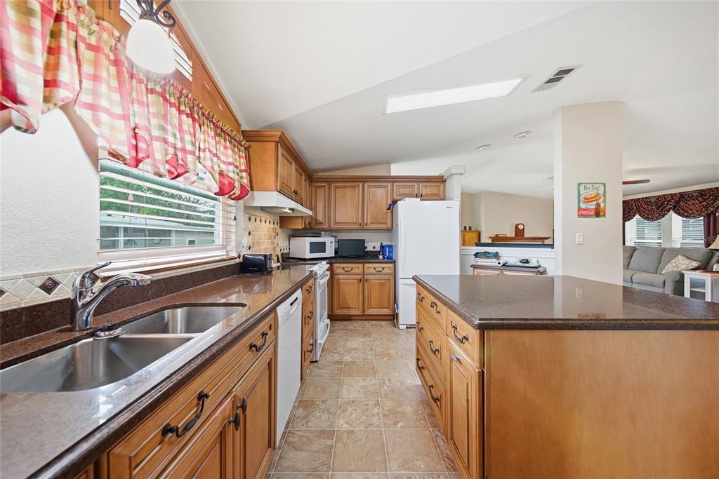 A kitchen features wood cabinets, dark countertops, a central island, and tile flooring — 8401 WEATHERFORD AVENUE, BROOKSVILLE, FL