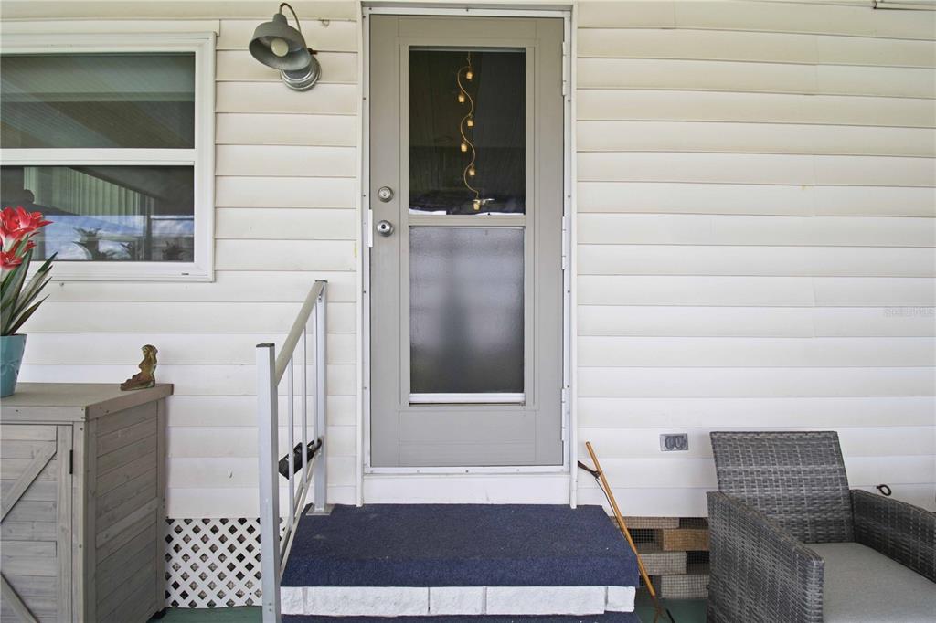 A gray storm door leads to a porch with white siding, a railing, and furniture — 5402 CHATEAU LANE, BRADENTON, FL