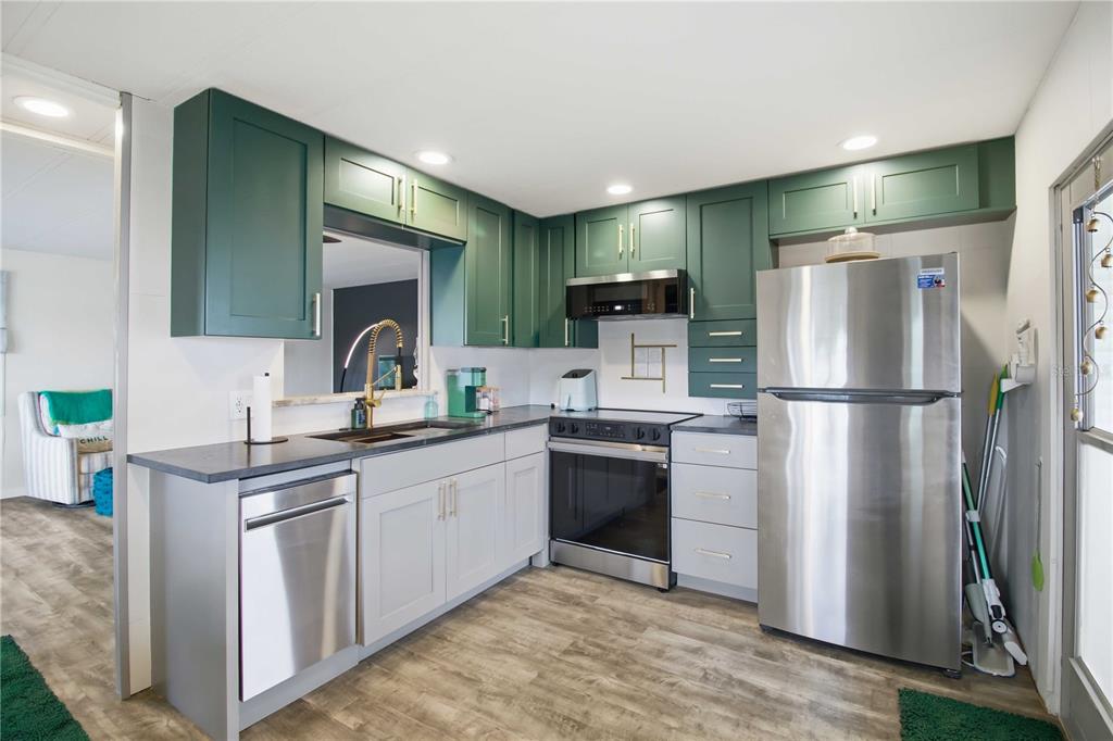 A kitchen features green upper cabinets, light gray lower cabinets, stainless steel appliances, and wood-look flooring — 5402 CHATEAU LANE, BRADENTON, FL