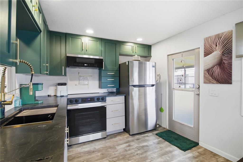 A kitchen features green cabinets, stainless steel appliances, dark countertops, and a glass-paneled door — 5402 CHATEAU LANE, BRADENTON, FL