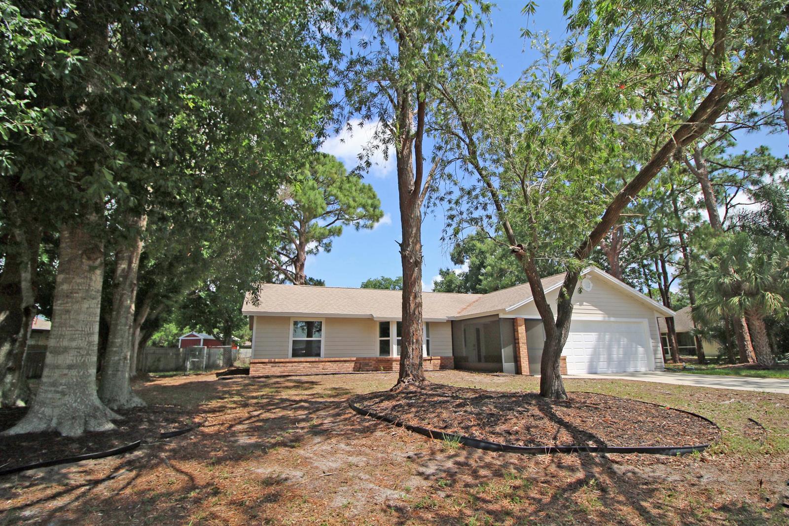 A single-story beige house with a brick base, a garage, and large trees in front — 271 Naylor NE, Palm Bay FL 32907, PALM BAY, FL