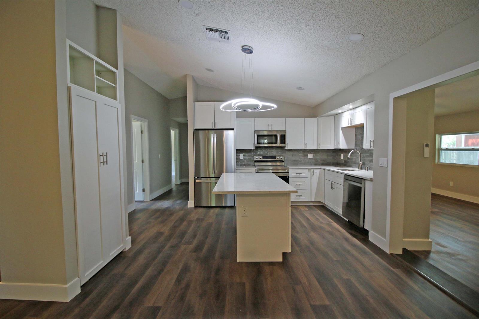 A modern kitchen features white cabinets, stainless steel appliances, a center island, and wood flooring — 271 Naylor NE, Palm Bay FL 32907, PALM BAY, FL