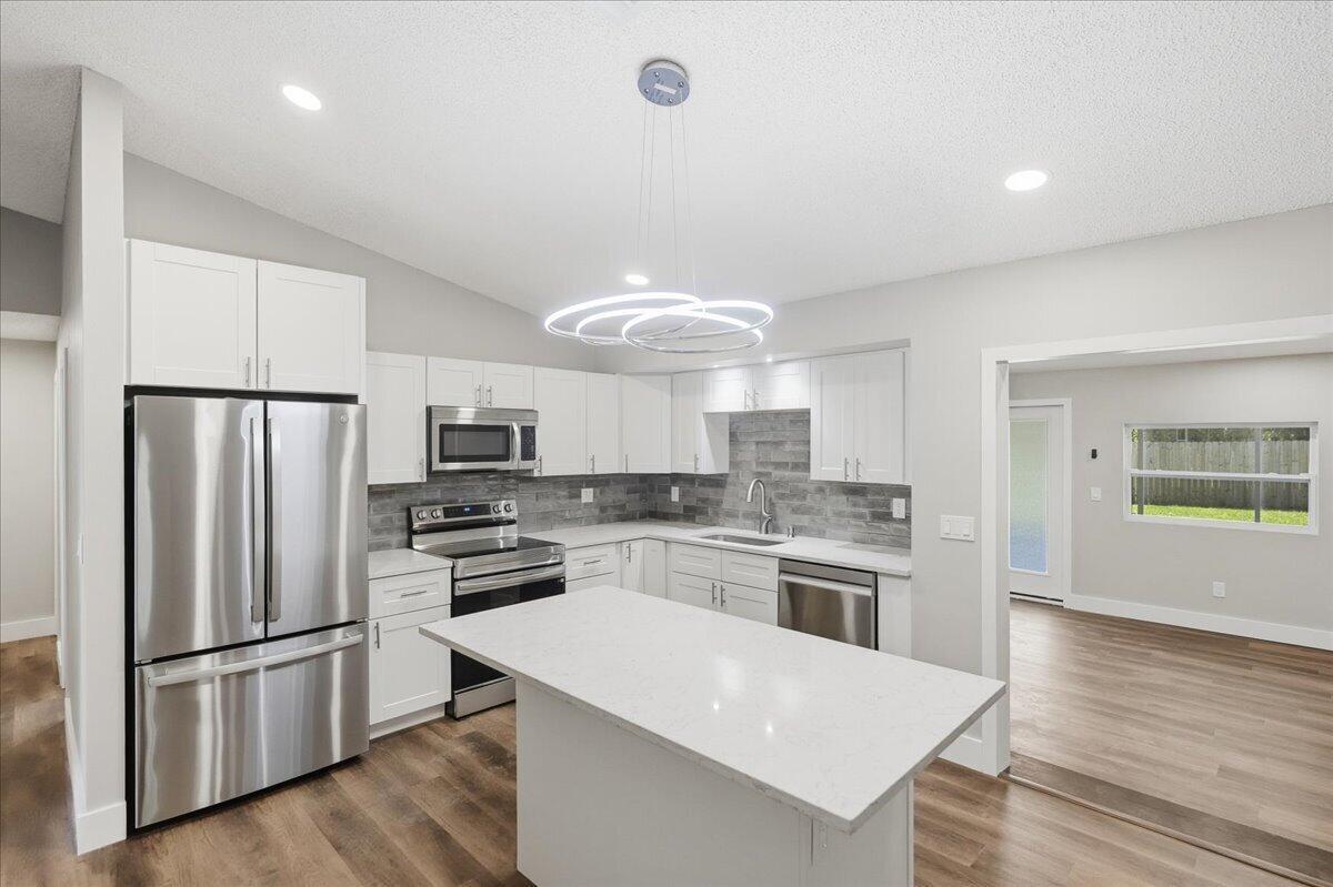 A modern kitchen features white cabinets, stainless steel appliances, a quartz island, and gray backsplash — 271 Naylor NE, Palm Bay FL 32907, PALM BAY, FL