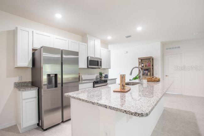 A kitchen features white cabinets, granite countertops, a stainless steel refrigerator, and a center island — 12898 SW 40TH TERRACE, OCALA, FL