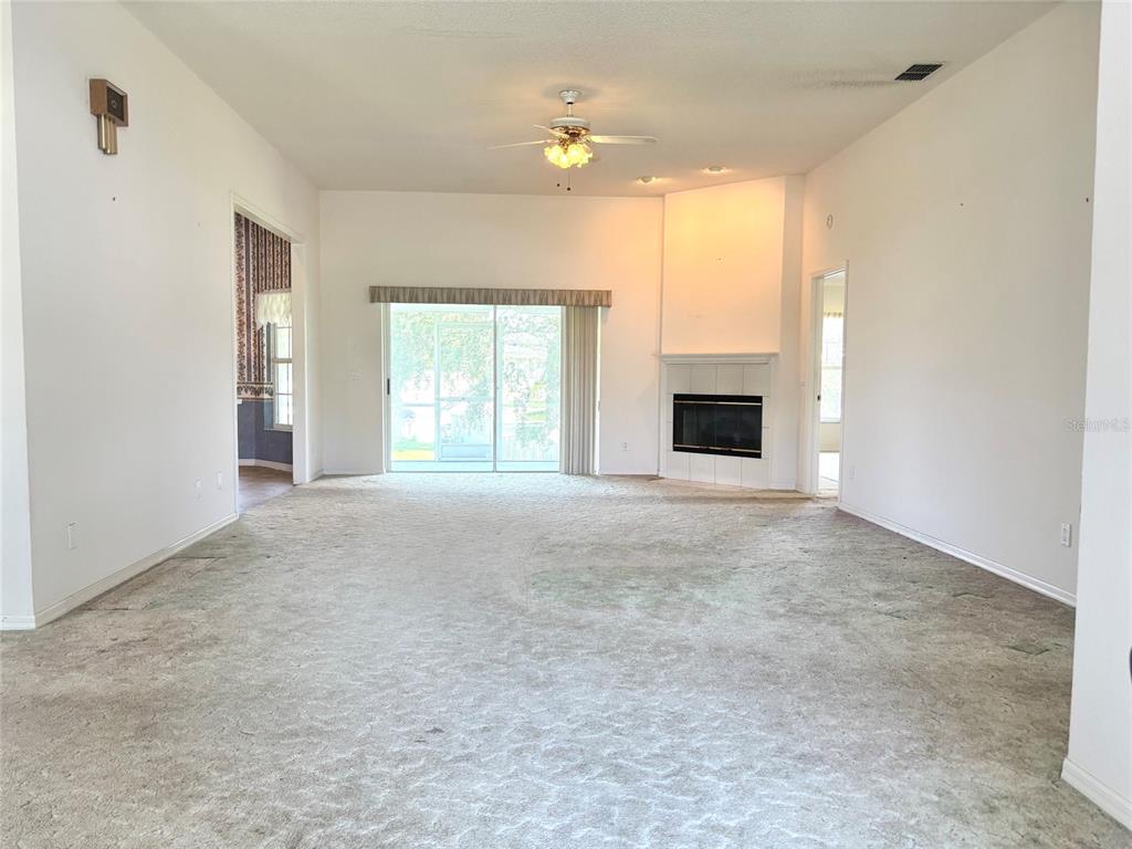 A spacious living room features beige carpeting, a corner fireplace, and sliding glass patio doors — 132 LAKE MARIAM WAY, WINTER HAVEN, FL