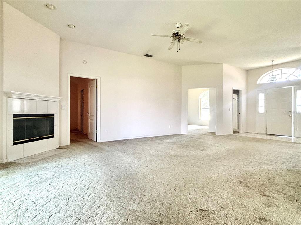 A spacious living room features beige carpeting, a white fireplace, and a ceiling fan — 132 LAKE MARIAM WAY, WINTER HAVEN, FL