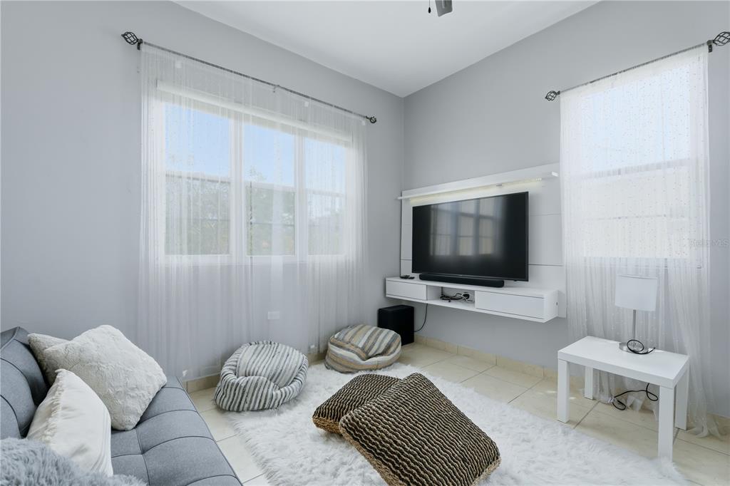 A living room features a wall-mounted television, a grey sofa, and floor cushions on tile — B-3 EVEREST, TOA ALTA, PR