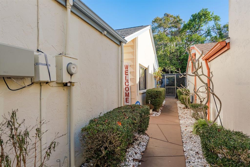A concrete walkway leads between two beige buildings toward a screened-in patio area — 12234 CIDER MILL LANE, HUDSON, FL