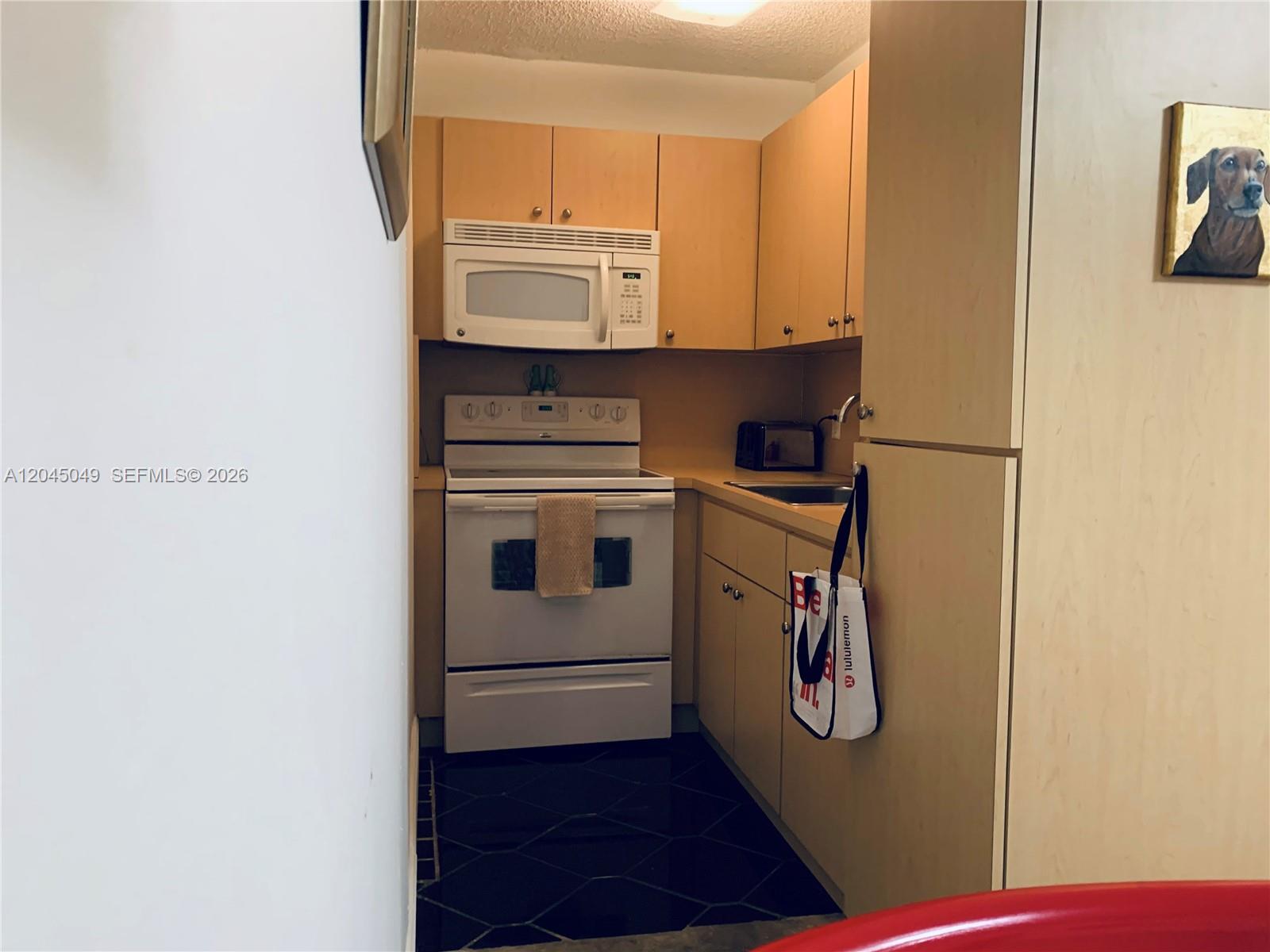 A small galley kitchen features light wood cabinets, white appliances, and dark tiled flooring — 11230 SW 138th St # A, Miami FL 33176, MIAMI, FL