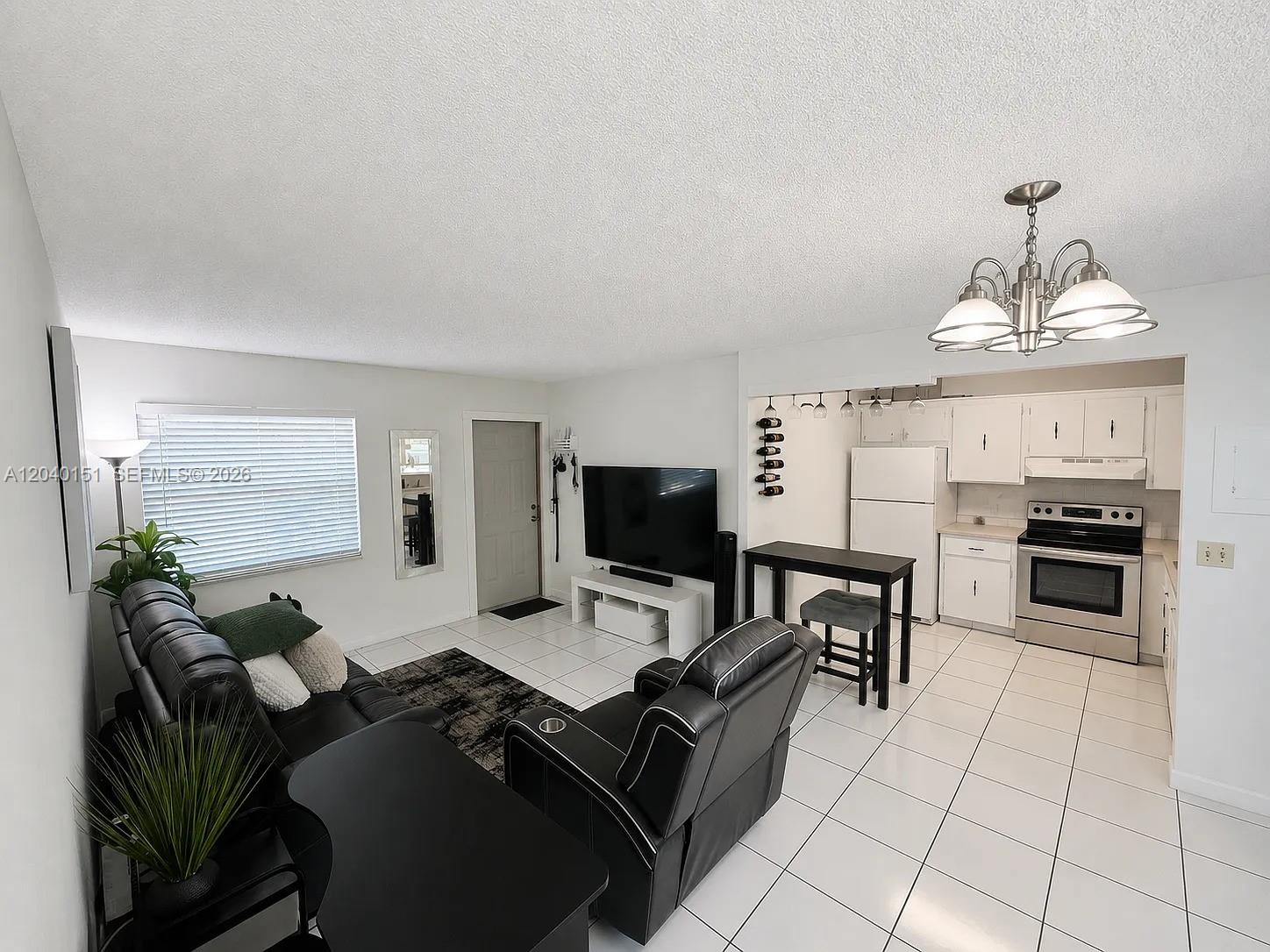An open-concept living room and kitchen featuring white tile floors and black leather furniture — 5771 SW 36th Ct # 301, Davie FL 33314, DAVIE, FL