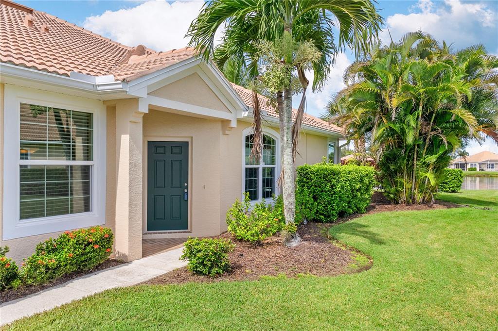 The exterior of a beige house features a dark green front door and palm trees — 5064 WHISPERING OAKS DRIVE, NORTH PORT, FL