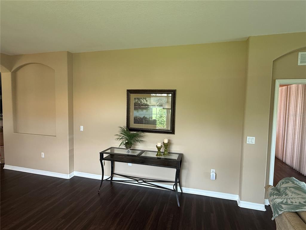 A living room features dark wood flooring, tan walls, a console table, and a framed picture — 5064 WHISPERING OAKS DRIVE, NORTH PORT, FL