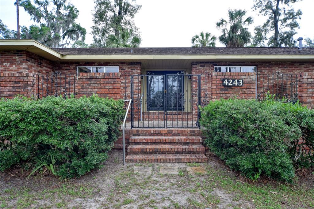 A brick house exterior features a gated entryway with steps and large green bushes — 4243 SE 8TH STREET, OCALA, FL