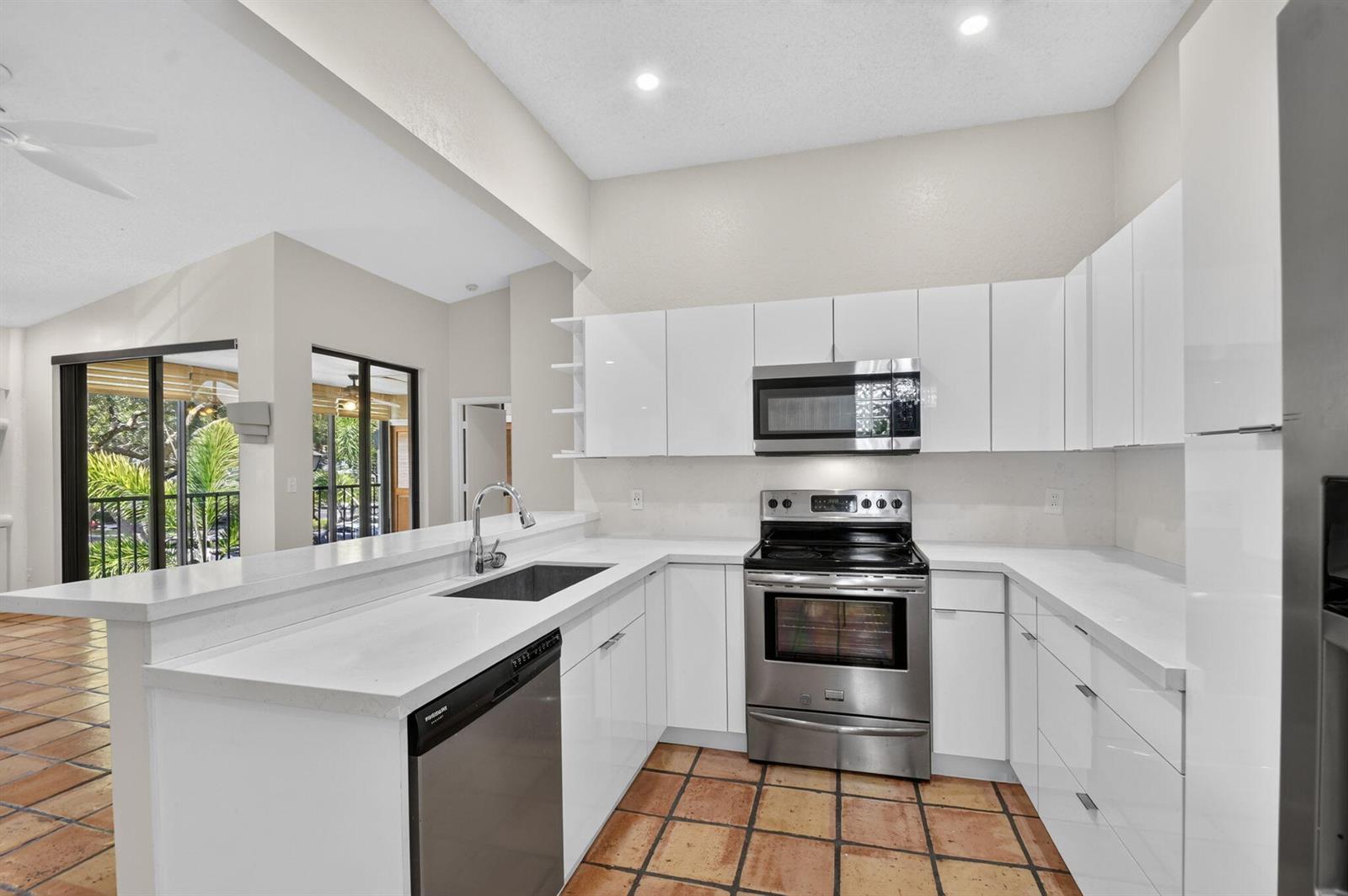 A kitchen features white flat-panel cabinets, stainless steel appliances, white countertops, and terracotta tile flooring — 5451 Verona Drive, Boynton Beach FL 33437, BOYNTON BEACH, FL