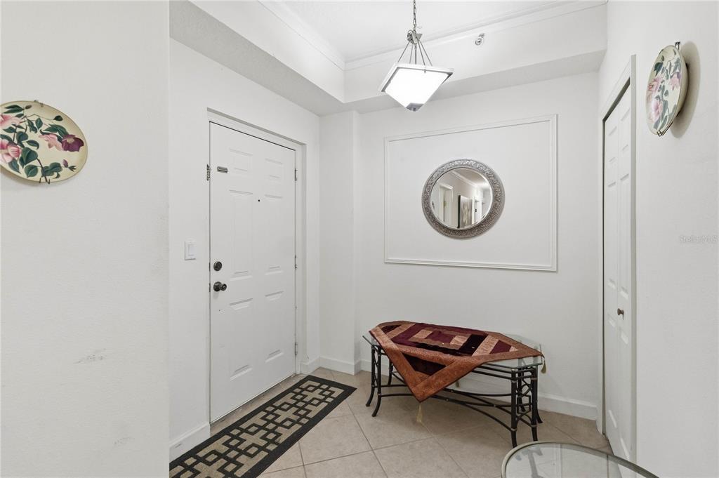 An entryway features tile flooring, a white door, a console table, and a circular wall mirror — 6336 BUFORD STREET UNIT 209, ORLANDO, FL