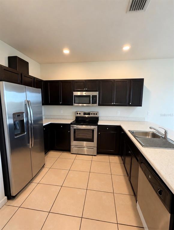 A kitchen features dark wood cabinets, stainless steel appliances, light countertops, and beige tile flooring — 11553 SW 248TH TERRACE, HOMESTEAD, FL