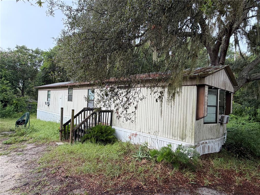 An exterior view of a weathered, single-wide mobile home with a wooden staircase — 12788 SE 102ND COURT, BELLEVIEW, FL