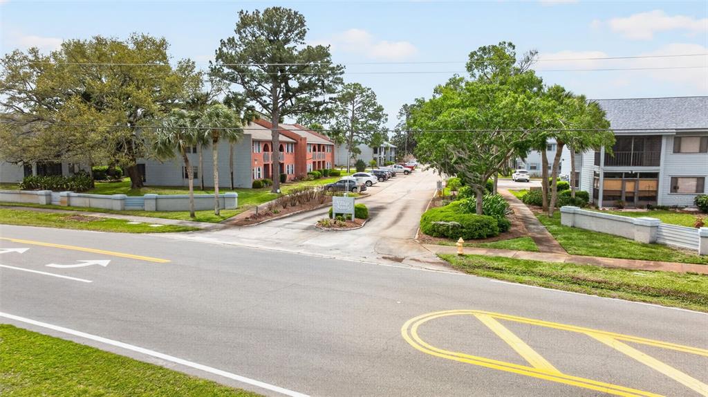 An exterior view shows the entrance to an apartment complex from a paved road — 1765 HARRISON STREET UNIT 204, TITUSVILLE, FL