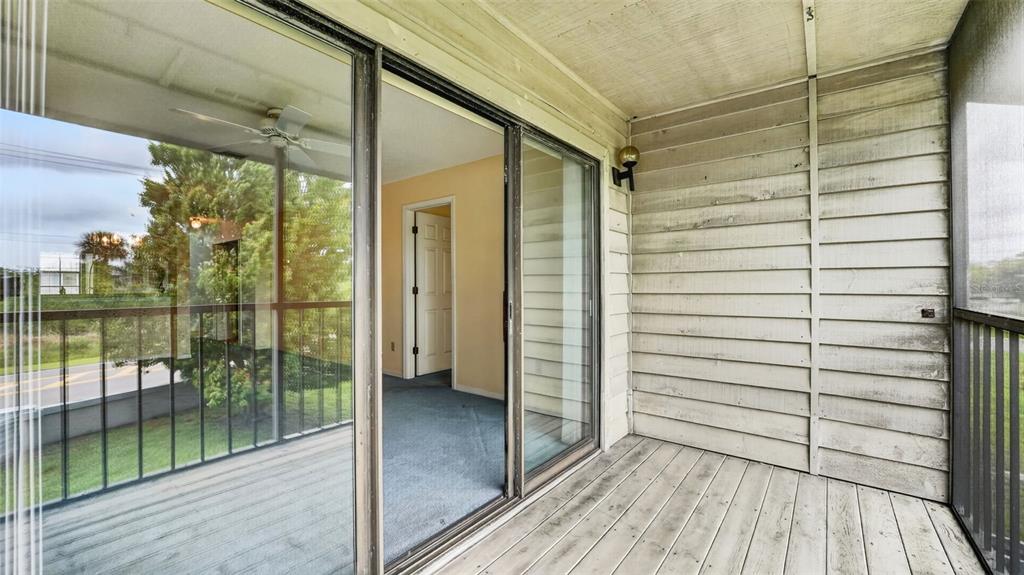 A screened-in porch with wood decking and siding overlooks a grassy area and road — 1765 HARRISON STREET UNIT 204, TITUSVILLE, FL