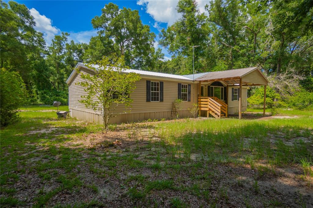 A tan manufactured home with a metal roof and a wooden porch sits among trees — 2349 NE 46TH CIRCLE, HIGH SPRINGS, FL