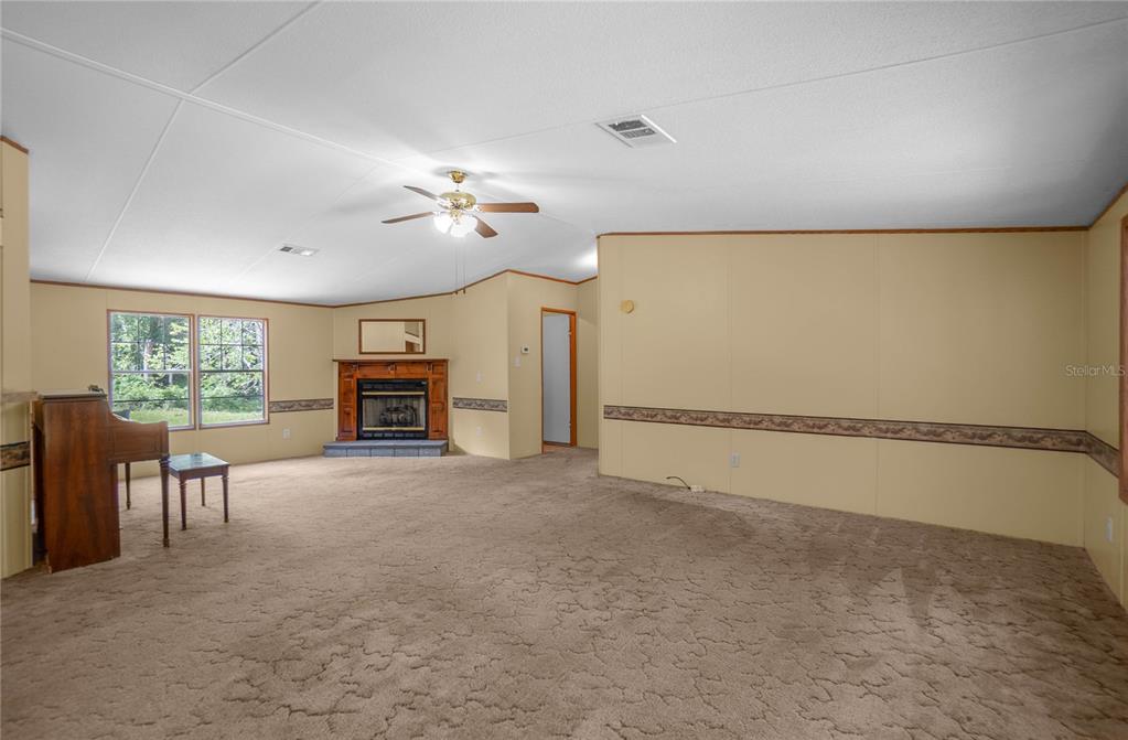 A spacious living room features beige carpet, tan walls, a fireplace, and a ceiling fan — 2349 NE 46TH CIRCLE, HIGH SPRINGS, FL