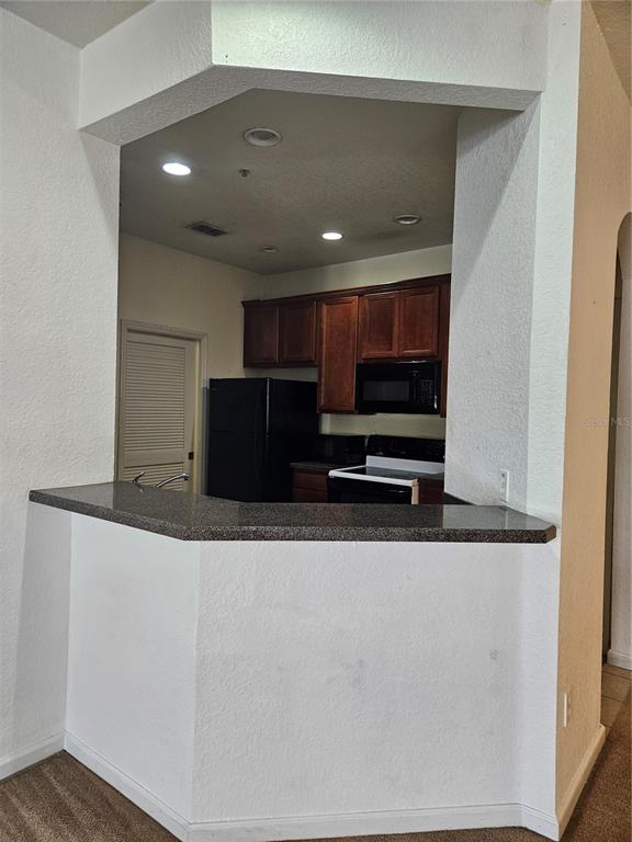 A kitchen with dark wood cabinets and black appliances is viewed over a breakfast bar — 3001 LAUREL PARK LANE UNIT 201, KISSIMMEE, FL