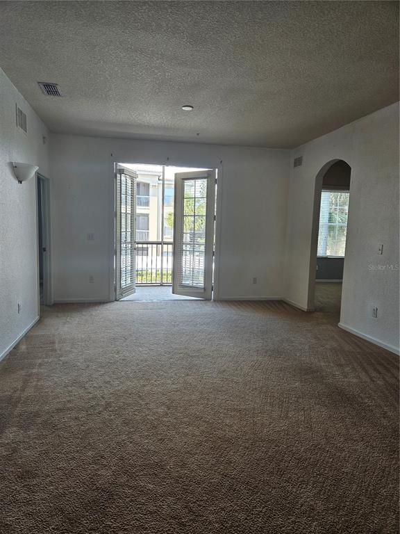 An empty carpeted living room features a glass door leading to a small balcony — 3001 LAUREL PARK LANE UNIT 201, KISSIMMEE, FL