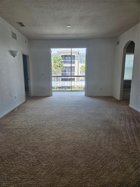 An empty living room features beige carpet, white walls, and a sliding glass door to a balcony — 3001 LAUREL PARK LANE UNIT 201, KISSIMMEE, FL