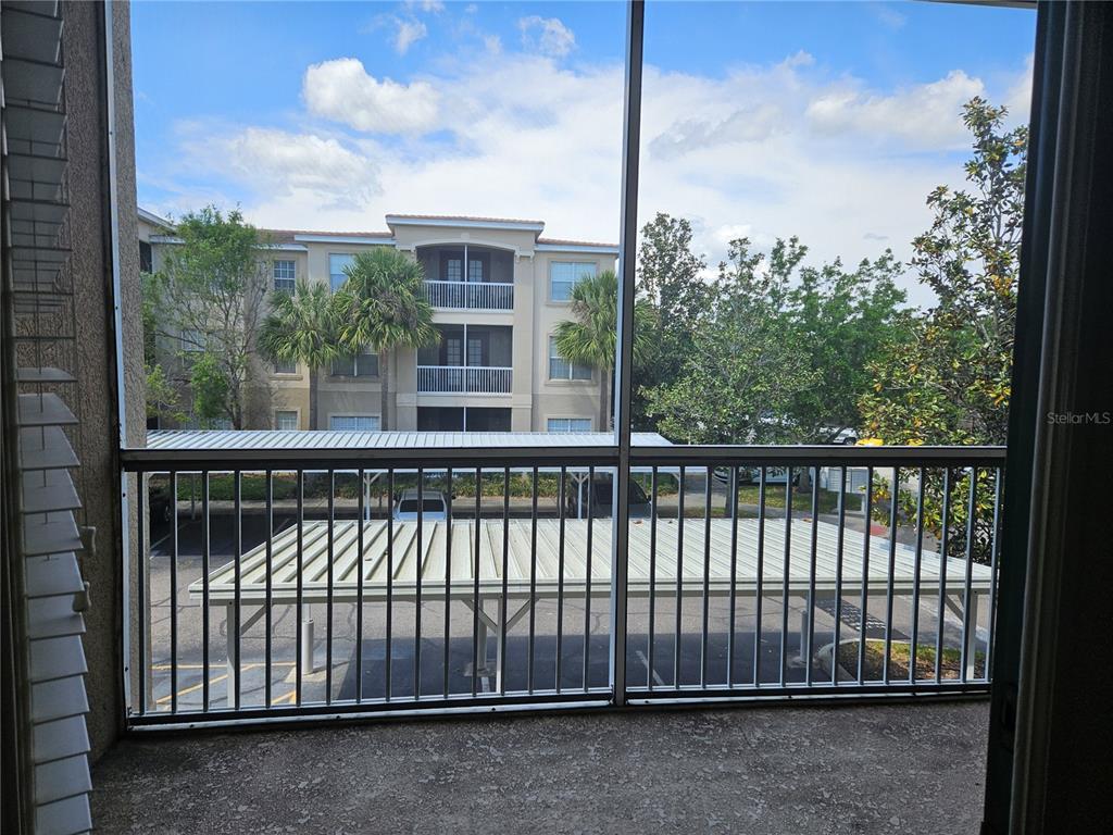 A view from a screened-in balcony overlooking a parking lot and a neighboring apartment building — 3001 LAUREL PARK LANE UNIT 201, KISSIMMEE, FL