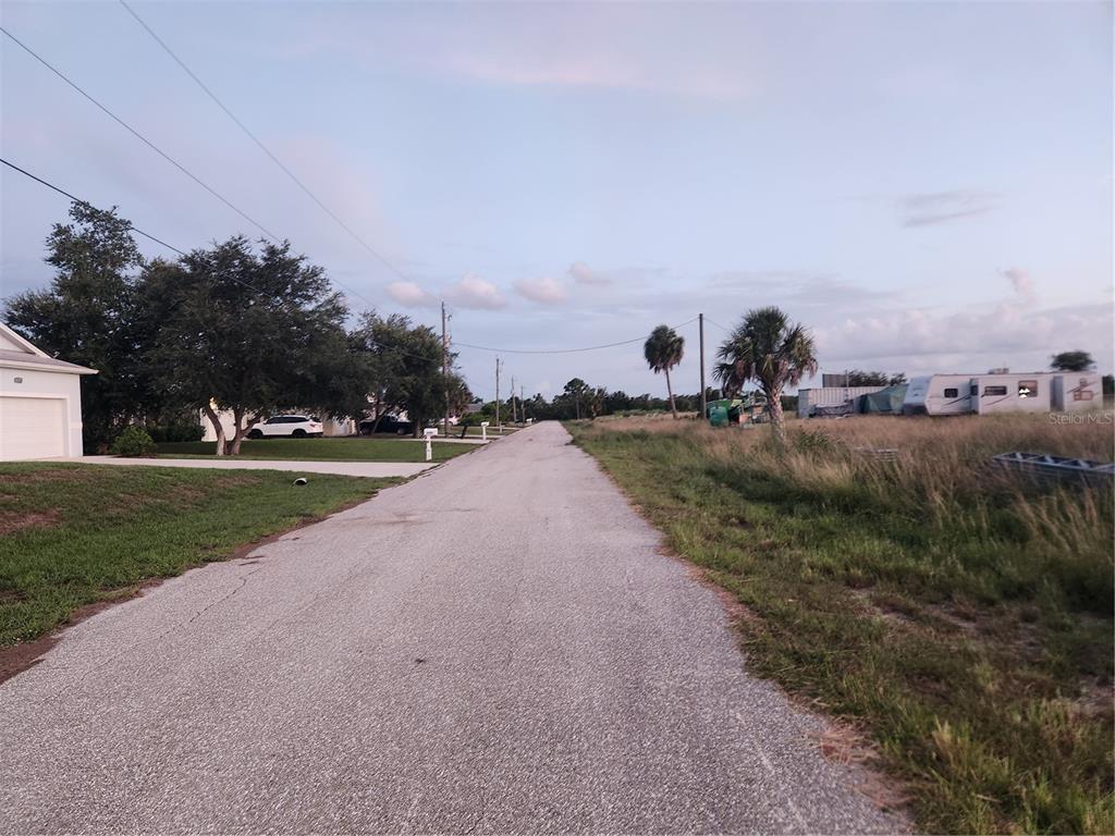 A paved road runs between a residential house and an undeveloped grassy lot — 2164 PEASLEY STREET, PORT CHARLOTTE, FL