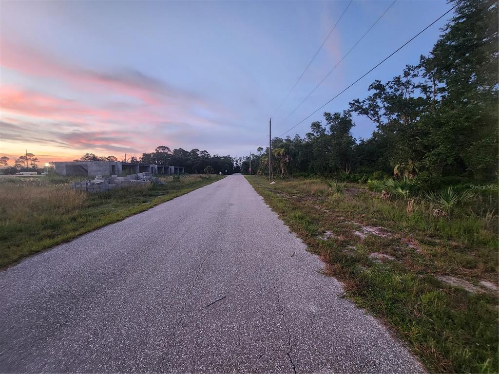 A paved road stretches toward the horizon past a construction site and wooded area — 2164 PEASLEY STREET, PORT CHARLOTTE, FL