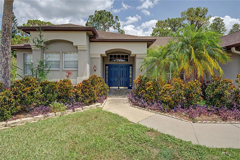 A beige house with a blue double front door and a landscaped front yard — 7201 FORESTEDGE COURT, NEW PORT RICHEY, FL