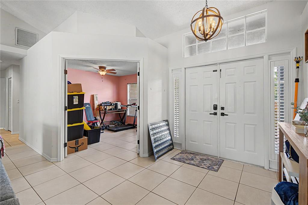 A tiled entryway features double front doors, a globe chandelier, and an adjacent workout room — 7201 FORESTEDGE COURT, NEW PORT RICHEY, FL