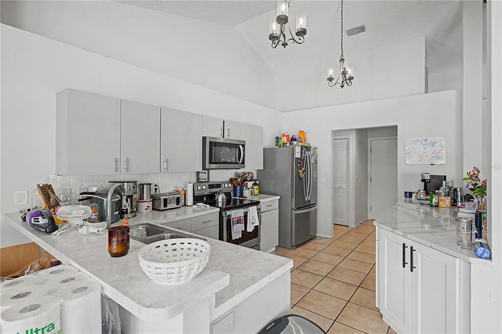 A kitchen features white cabinets, stainless steel appliances, a breakfast bar, and tile flooring — 7201 FORESTEDGE COURT, NEW PORT RICHEY, FL