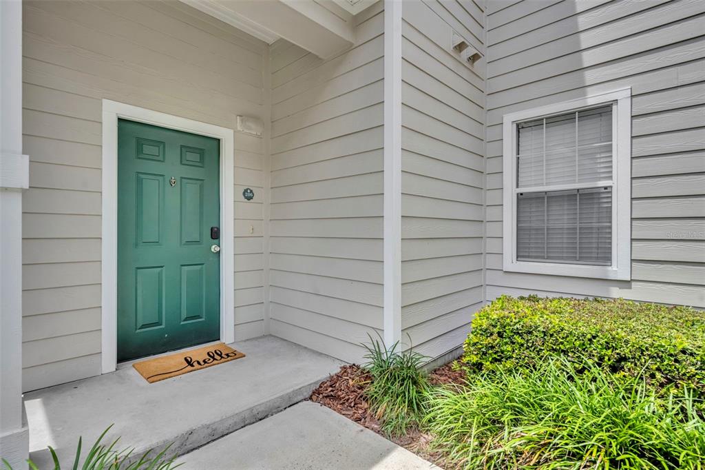 A green front door with a hello mat sits on a concrete porch beside siding — 200 SOUTHERN PECAN CIRCLE UNIT 206, WINTER GARDEN, FL