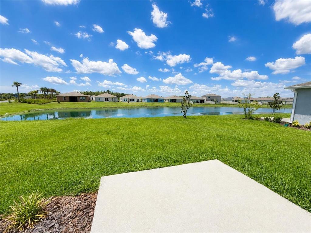 A concrete patio overlooks a grassy backyard and a small pond with houses in the distance — 5632 LOGGIA LANE, KISSIMMEE, FL