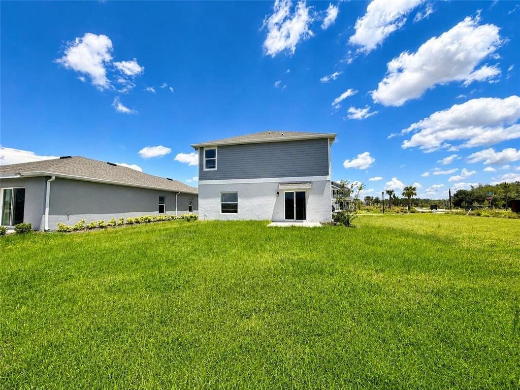 The rear exterior of a two-story house features gray siding, white stucco, and a lawn — 5632 LOGGIA LANE, KISSIMMEE, FL
